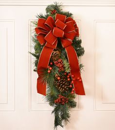 a christmas wreath with pine cones and red ribbon hanging on the front door to welcome guests