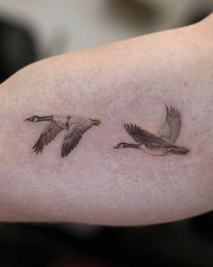 two birds flying next to each other on a person's left arm with tattoos