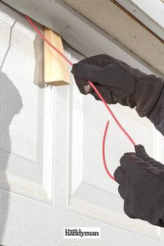 two hands in black gloves are holding a red cord to the side of a white door