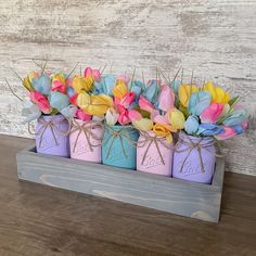 four mason jars filled with colorful flowers on top of a wooden table next to a wall