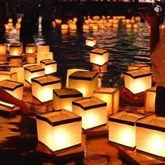 many lanterns floating in the water with people standing around them and one person holding a cell phone