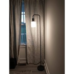 a floor lamp in front of a window next to a rug on the floor and an area rug