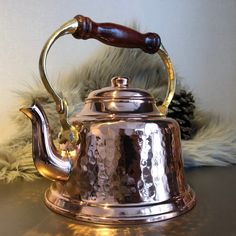 a metal tea kettle with a wooden handle on a table next to a pine cone