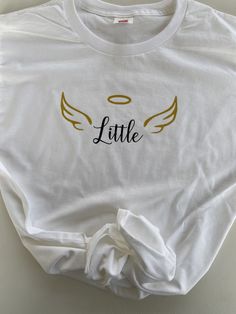 a white shirt with gold angel wings and the word little on it