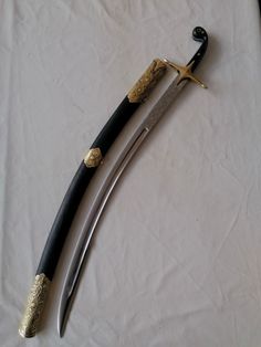 two black and gold colored swords laying on top of a white cloth covered tablecloth