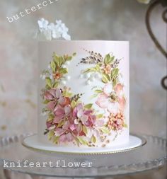 a white cake decorated with pink flowers and green leaves on a glass platter that says, buttercretche