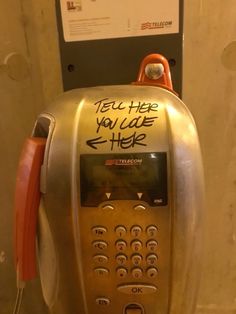 an old style pay phone with graffiti on the front and back panel, attached to a wall