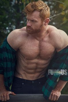 a shirtless man leaning on a fence looking at the camera with his hands in his pockets