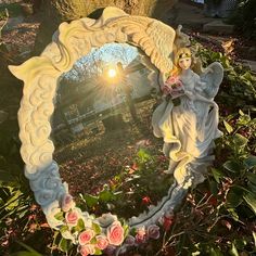 an angel figurine sitting on top of a mirror in the middle of flowers