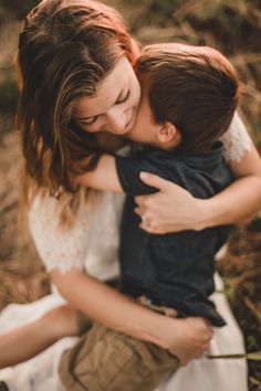 a woman holding a young boy in her arms while he is kissing him on the cheek