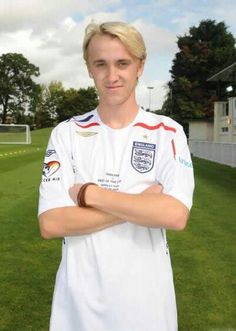 a man standing in front of a soccer field with his arms crossed and looking at the camera