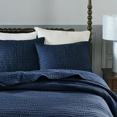 a bed with blue bedspread and two pillows on top of it, next to a night stand