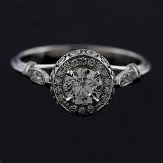 a white gold ring with an old cut diamond surrounded by small round diamonds on a black background