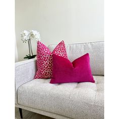 two pink and red pillows sitting on top of a couch next to a vase with flowers