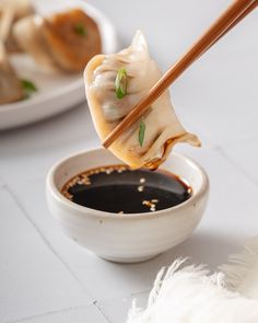 a person holding chopsticks over a bowl of food with dipping sauce in it