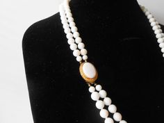 "A vintage white necklace. This is a beautiful necklace of summer white beads. The white bead necklace is a double strand of uniform size white beads, It is hand tied between each bead to prevent spillage. The necklace has a tab insert closure. This closure has a white cabochon in a goldtone setting. A beautiful summer necklace. MATERIAL: Beads CONDITION: Good SIZE: 28\" in length COLOR: White" Classic White Beaded Pearl Necklace, Classic White Beaded Necklaces, Classic White Beaded Necklace, Vintage Double Strand White Jewelry, Vintage White Double Strand Jewelry, Vintage White Double Strand Pearl Necklace, White Beaded Pearl Necklace With Oval Beads, White Oval Beaded Pearl Necklace, Vintage White Single Strand Beaded Necklaces