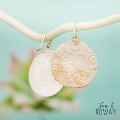 two silver and gold earrings hanging from a white hook on a twig with flowers in the background