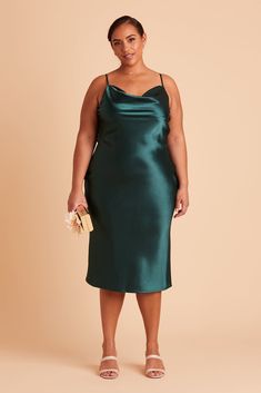 a woman in a dark green dress with her hands on her hips, posing for the camera