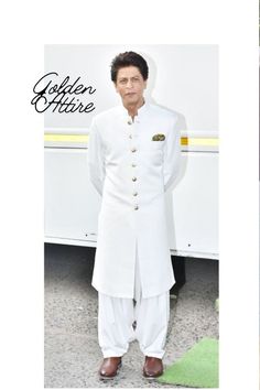 the man is wearing a white suit and standing in front of a bus with his hands on his hips