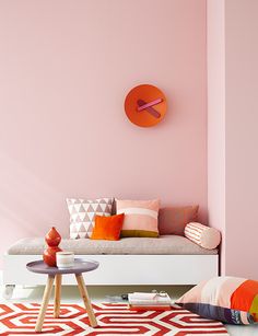 a living room with pink walls and pillows on the couch in front of a clock