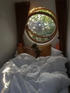 a woman laying in bed under a round window