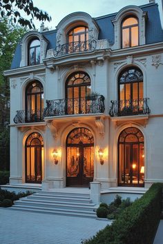 Elegant mansion with illuminated arched windows and decorative wrought iron. Check out the whimsical wonders of big houses where vastness meets imagination, transforming envy into inspiration! Elegant Mansion, Suburban House, Stone Facade, French Architecture, Huge Windows, Modern Mansion, Wrap Around Porch, Cozy Farmhouse, Two Story Homes