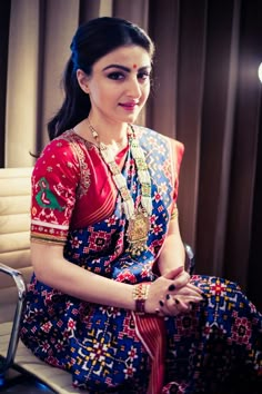 a woman sitting on top of a chair wearing a colorful dress and holding a necklace