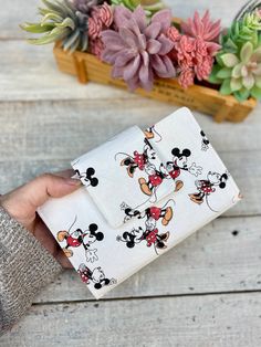 a person holding a mickey mouse wallet on top of a wooden table with succulents in the background