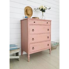 a pink dresser sitting next to a white wall with flowers on it and a straw hat on top