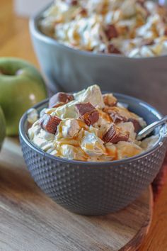 two bowls filled with food sitting on top of a wooden cutting board next to an apple