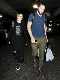 a man and woman walking through an airport holding hands with one another as they both carry bags