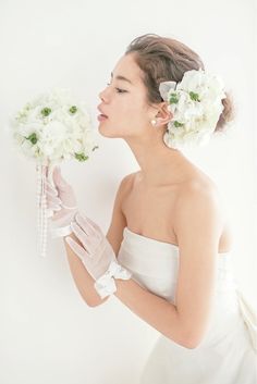 a woman in white dress holding flowers with her face close to the camera and wearing gloves