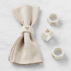 three napkin rings and two napkin holders on a white table with a beige linen bag