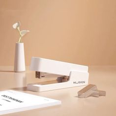 a white vase with a flower in it next to a stapler and some papers