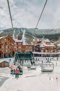 skiers and snowboarders at the bottom of a ski lift in front of a resort