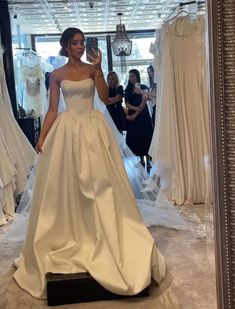 a woman taking a selfie in front of wedding gowns on mannequins