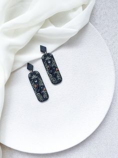 two black and white earrings sitting on top of a white plate next to a white cloth