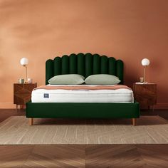 a bed with green headboard and pillows in a pink walled room next to two nightstands