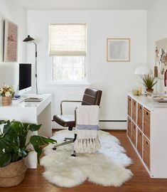 a white room with a chair, desk and plants in the corner on the floor