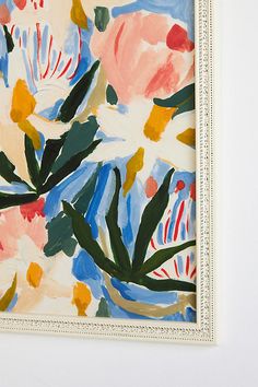 a painting on the wall with flowers painted in different colors and shapes, hanging from a white frame