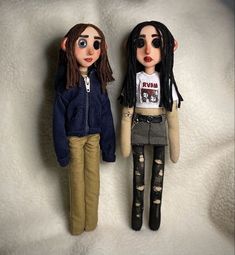 two dolls standing next to each other on a white surface, one with long hair and the other with dreadlocks