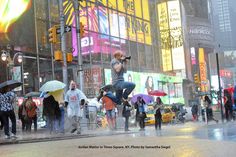 a man jumping in the air with an umbrella on a busy city street at night