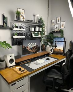 an office desk with a computer, speakers and plants on it in front of a window