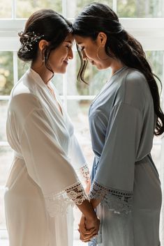 two women standing next to each other in front of a window holding hands and looking at each other