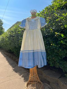 a blue and white dress is hanging on a wire basket in front of some bushes