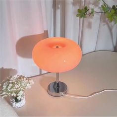 an orange lamp sitting on top of a table next to a vase filled with flowers