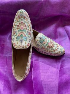 pair of white shoes with floral design on purple cloth