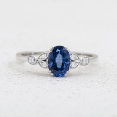 an oval blue sapphire and diamond ring on a white surface with three diamonds around it