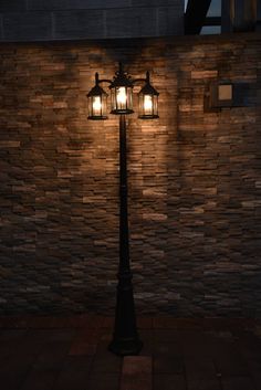 a lamp post with two lights on it in front of a brick wall at night