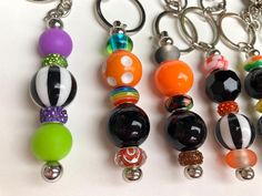 four different colored beads are attached to key chains on a white surface, one is black and the other is orange